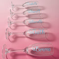 Set of personalized champagne flutes with names on a pink background
