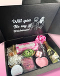 Gift box with 'Will you be my Bridesmaid?' message and various items including a bottle of champagne.