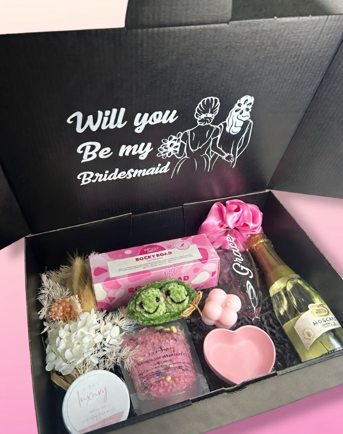 Gift box with 'Will you be my Bridesmaid?' message and various items including a bottle of champagne.